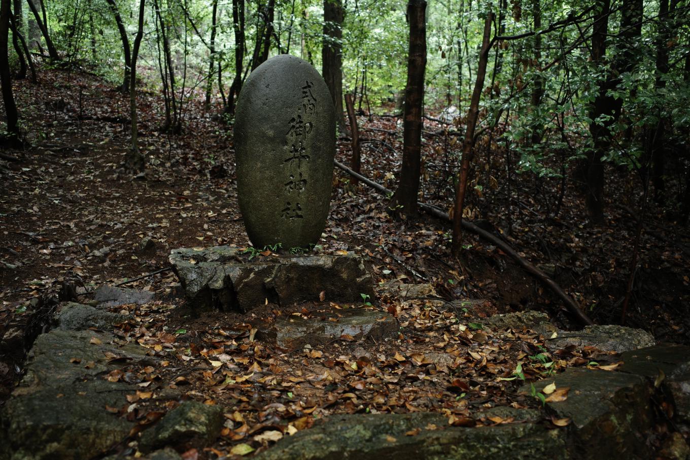薄暗い樹林にある御井神社の旧社地を示す石碑。