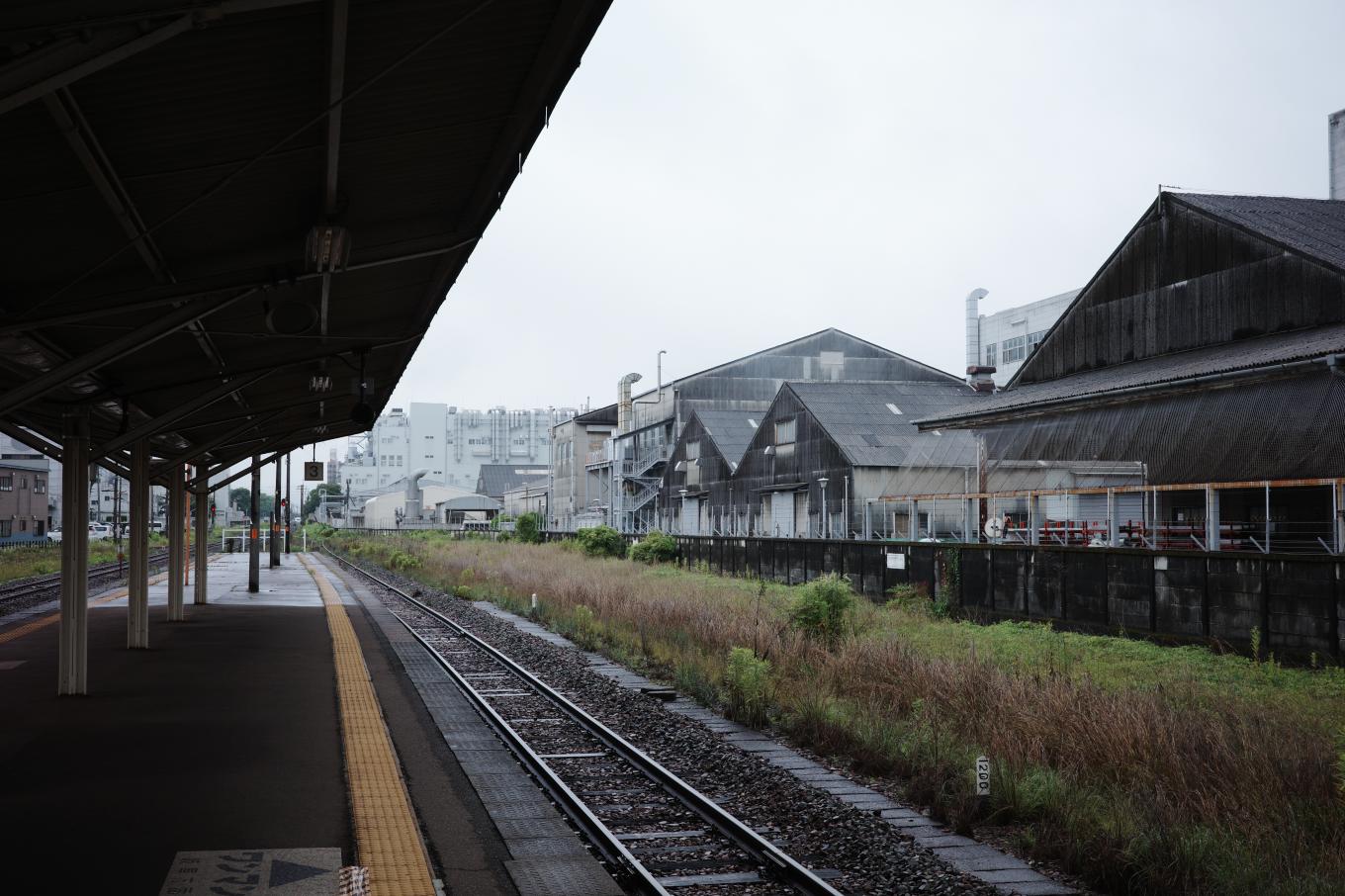 駅裏の貨物側線跡らしき空き地と、その向こうに広がる川崎重工の工場。